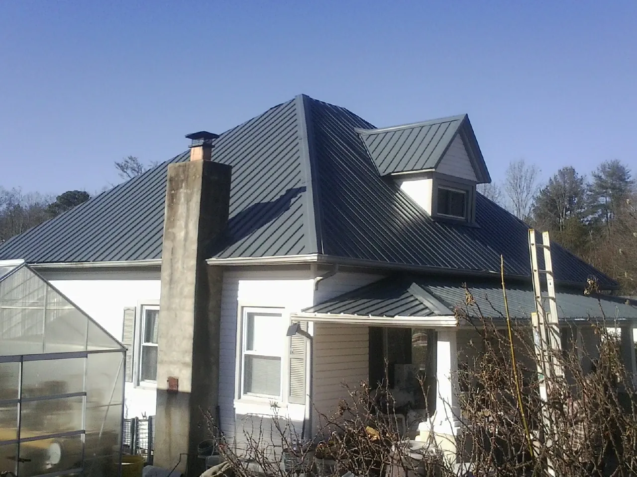 Dark blue standing seam metal roof on a white farmhouse with dormer — Slate & Tile Roof Repair by Roofing Brothers in Shepherd