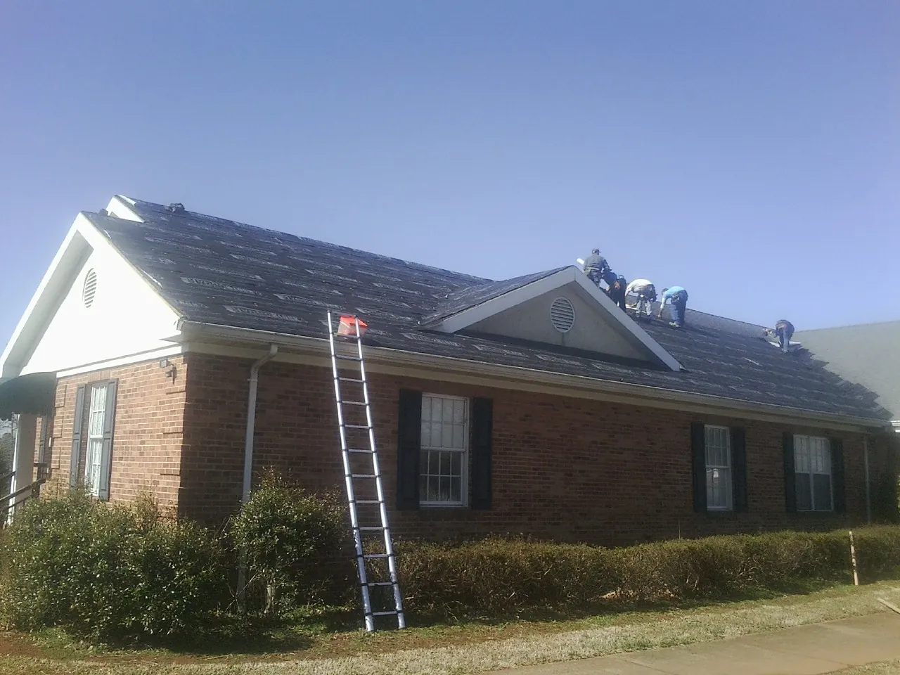 Crew tearing shingles off a brick ranch roof with a ladder set — Emergency Roof Repair work by our crew in Shepherd