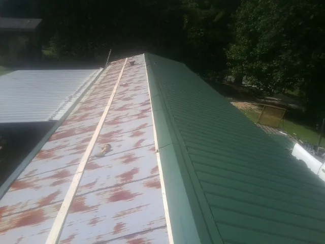 Old rusted panels beside newly installed green metal roofing — Wind Damage Roof Repair by Roofing Brothers in Shepherd
