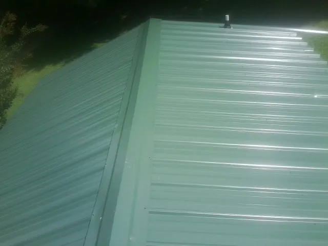 New green metal panels meeting at the ridge of a roof — Flat Roof Repair work by our crew in Shepherd