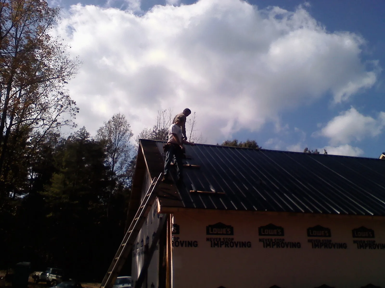 Roofer fastening dark metal panels high against a cloudy sky, from a Roof Inspection job in Shepherd