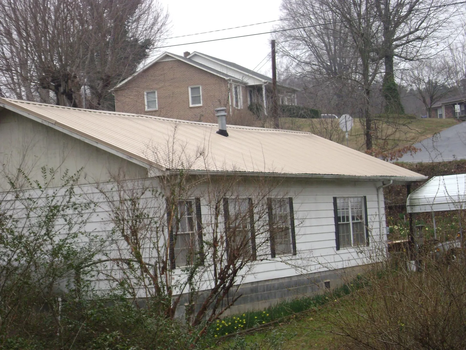 Tan metal roof on a white sided house set into a hillside — Commercial Roofing by Roofing Brothers in Shepherd